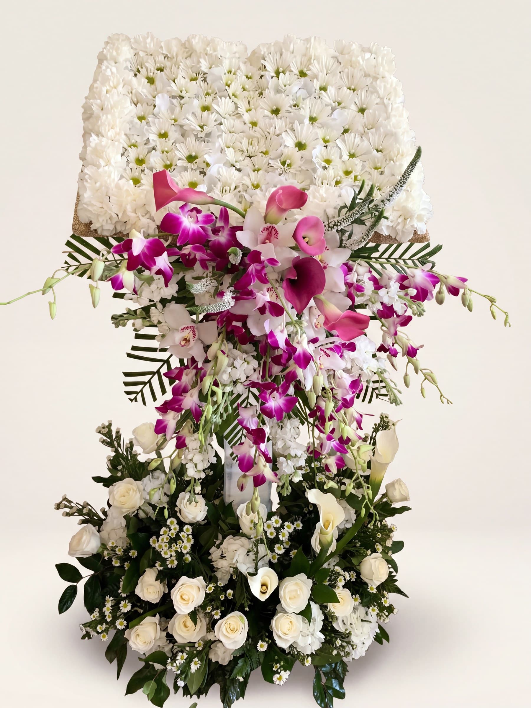 Tall funeral tribute with a white floral top, a cascade of fuchsia orchids, and a base of white roses and calla lilies