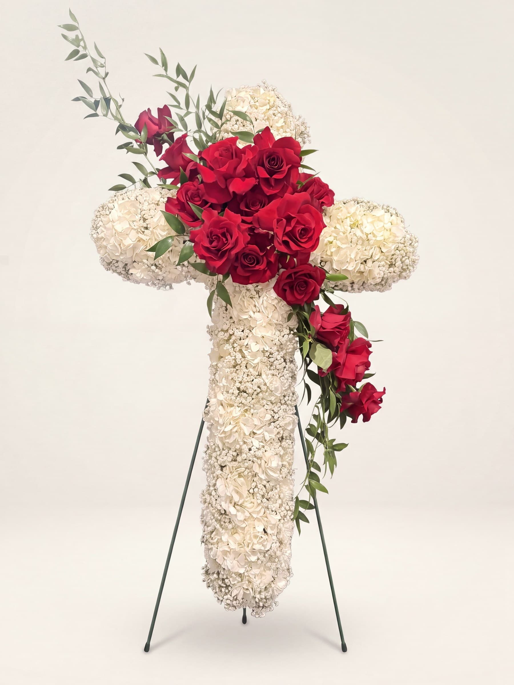 Standing funeral cross of white hydrangea and baby's breath with a cluster and cascade of red roses on an easel