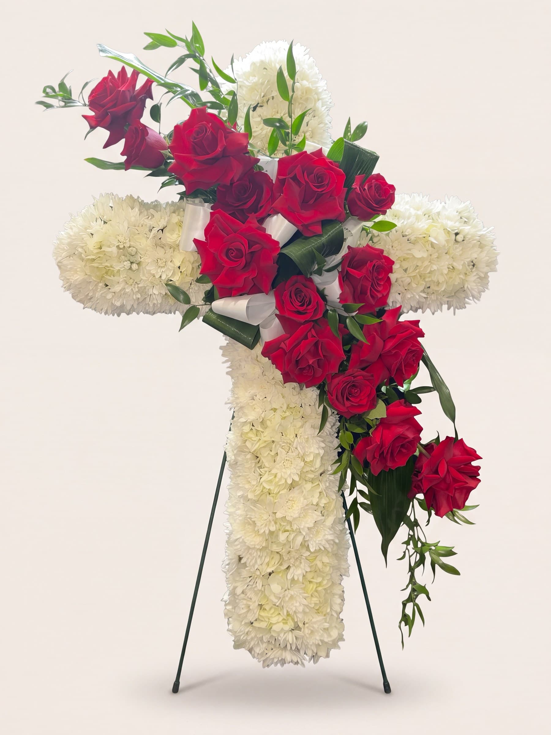 Standing funeral cross of white chrysanthemums with a cascade of red roses on an easel