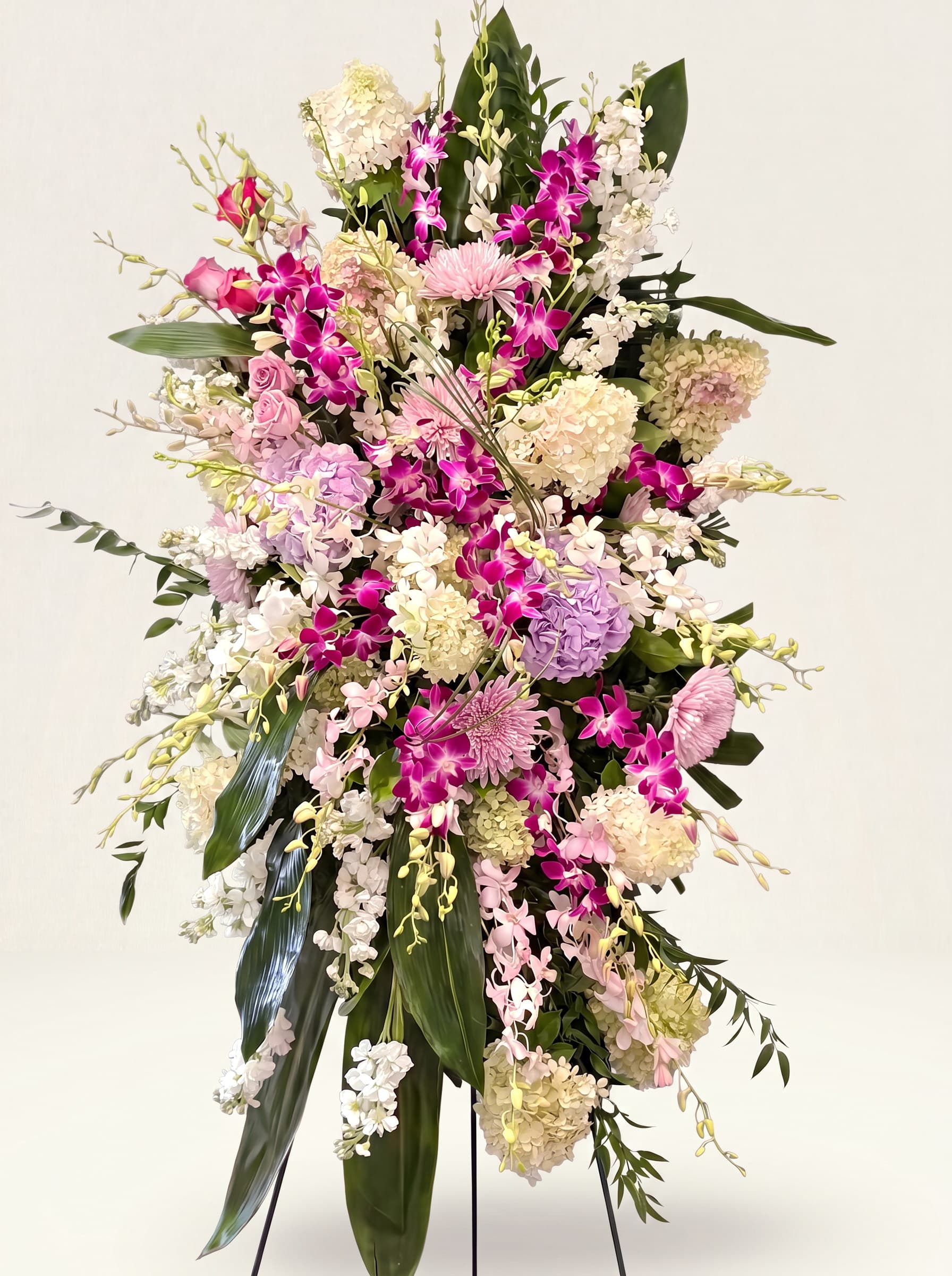 Tall standing funeral spray of purple dendrobium orchids, lavender roses, and white hydrangea