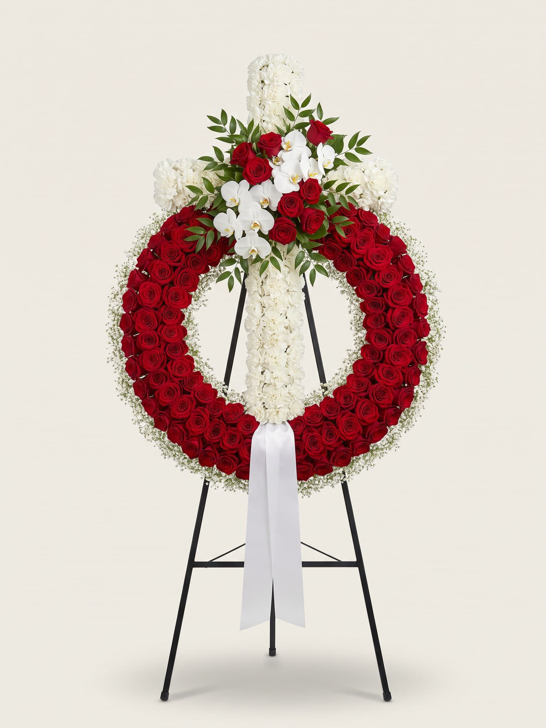 Standing funeral wreath of red roses with a white carnation cross and white orchids on an easel