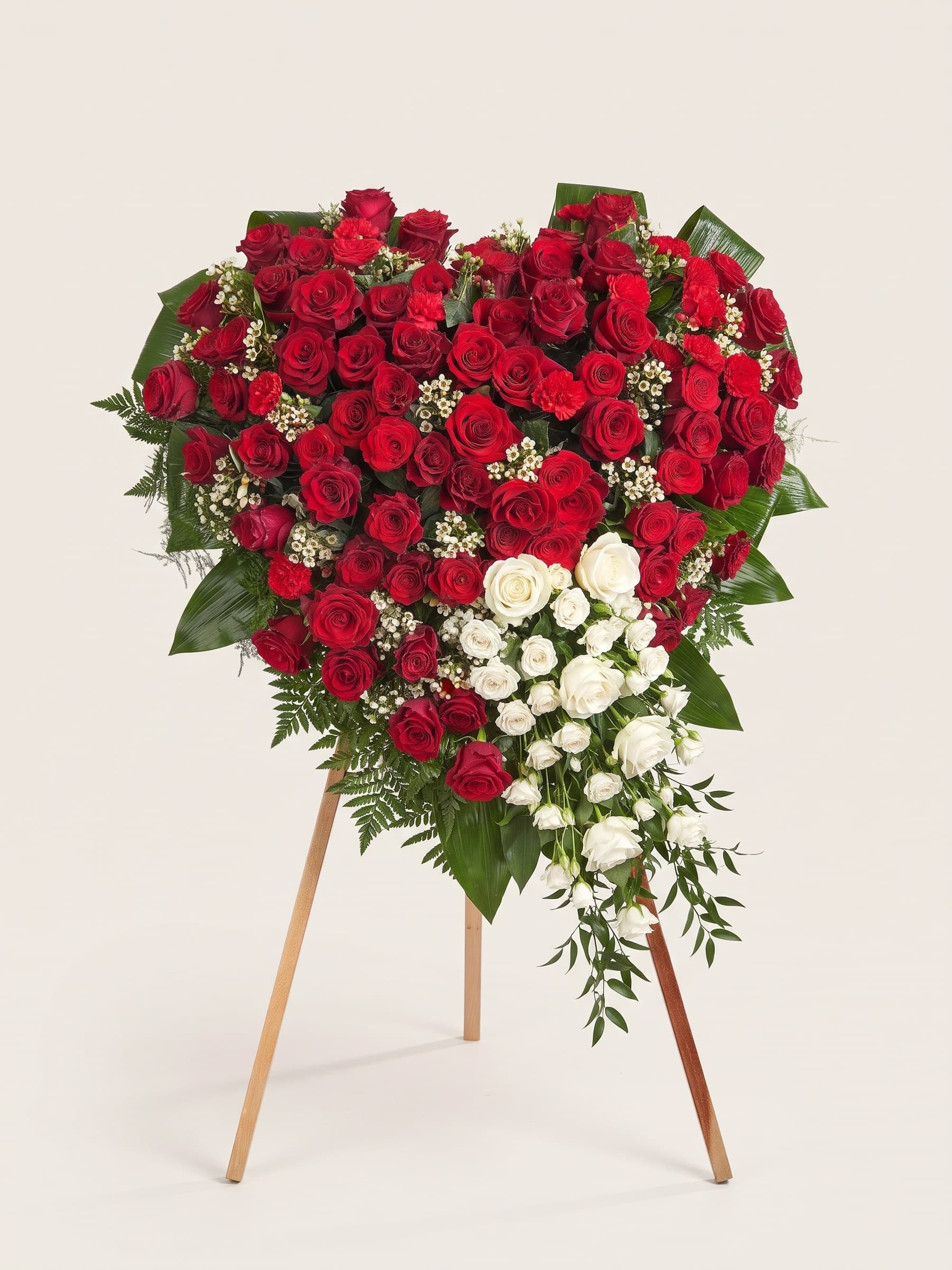 Standing funeral heart of 100 red roses with a cascade of white roses on a wooden easel