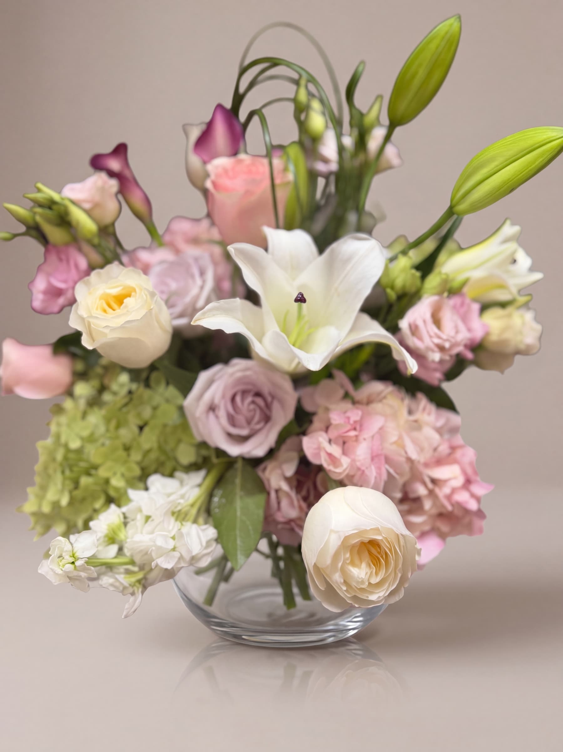 Arreglo de lirios blancos, rosas malva y hortensia rosa antiguo en cuenco de vidrio transparente