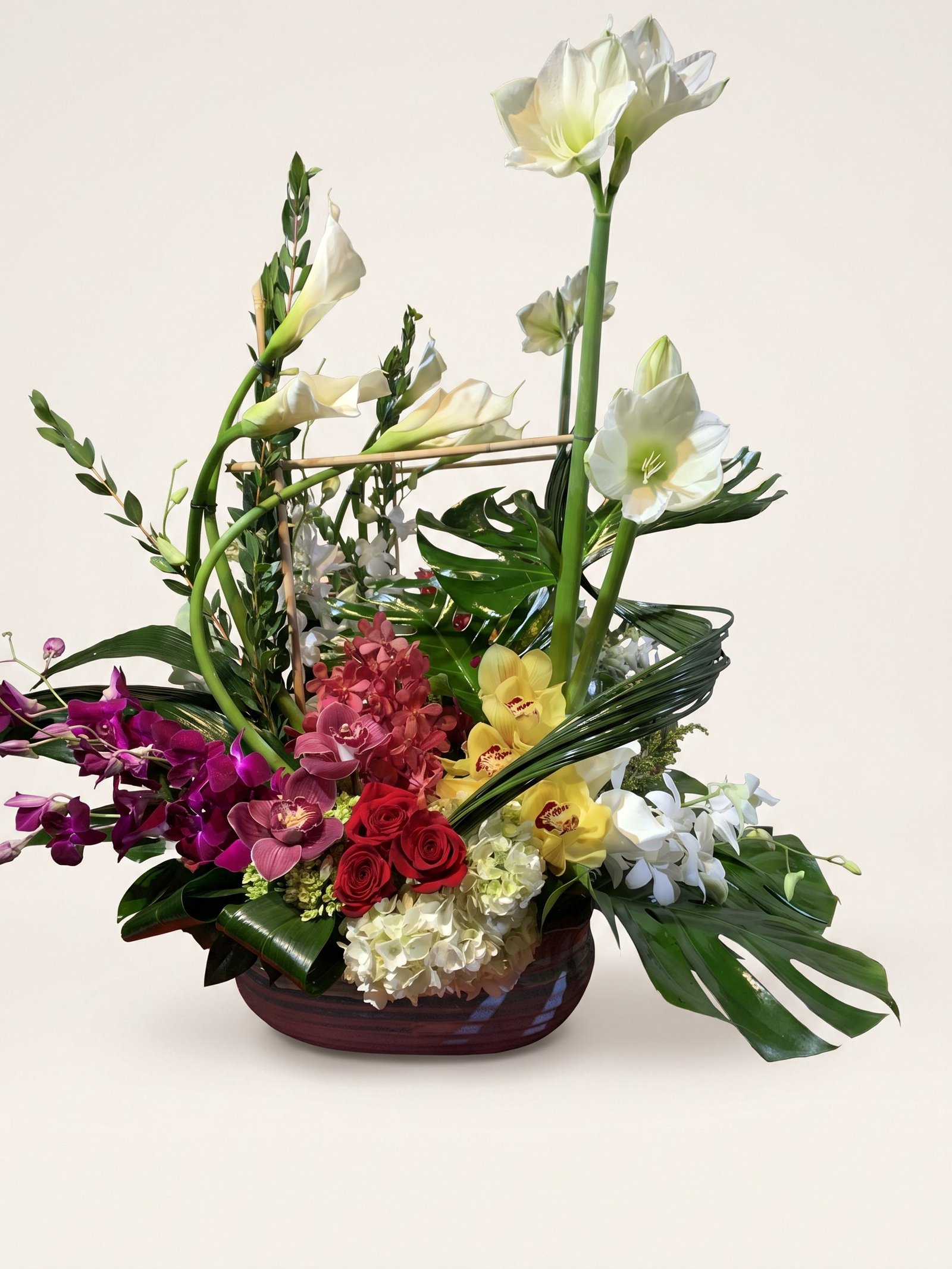 Amaryllis blanco alto con orquídeas cymbidium rojas y amarillas y rosas rojas en cuenco bajo oscuro