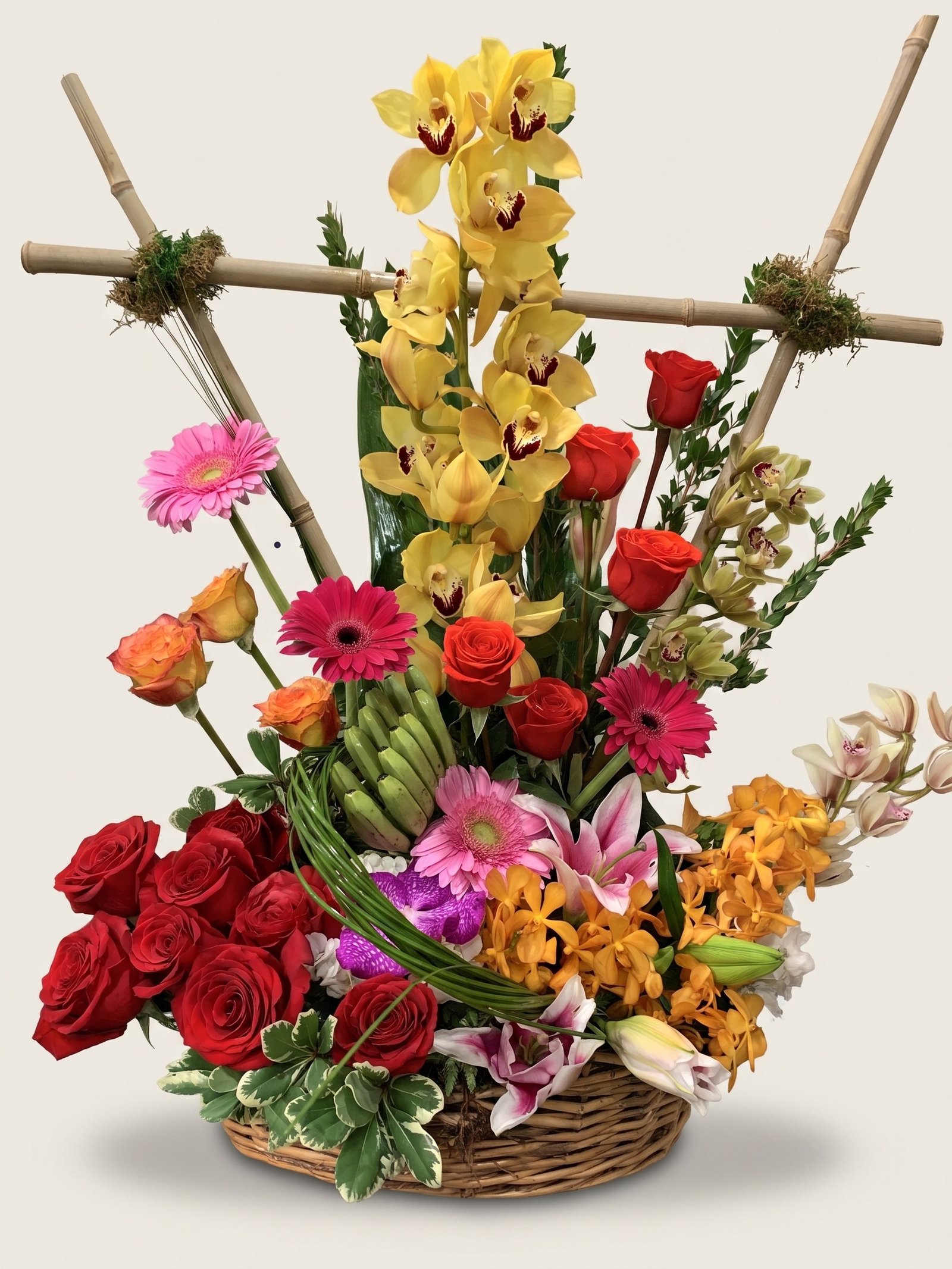 Orquídeas cymbidium amarillas sobre bambú con gerberas y rosas en cesta de mimbre