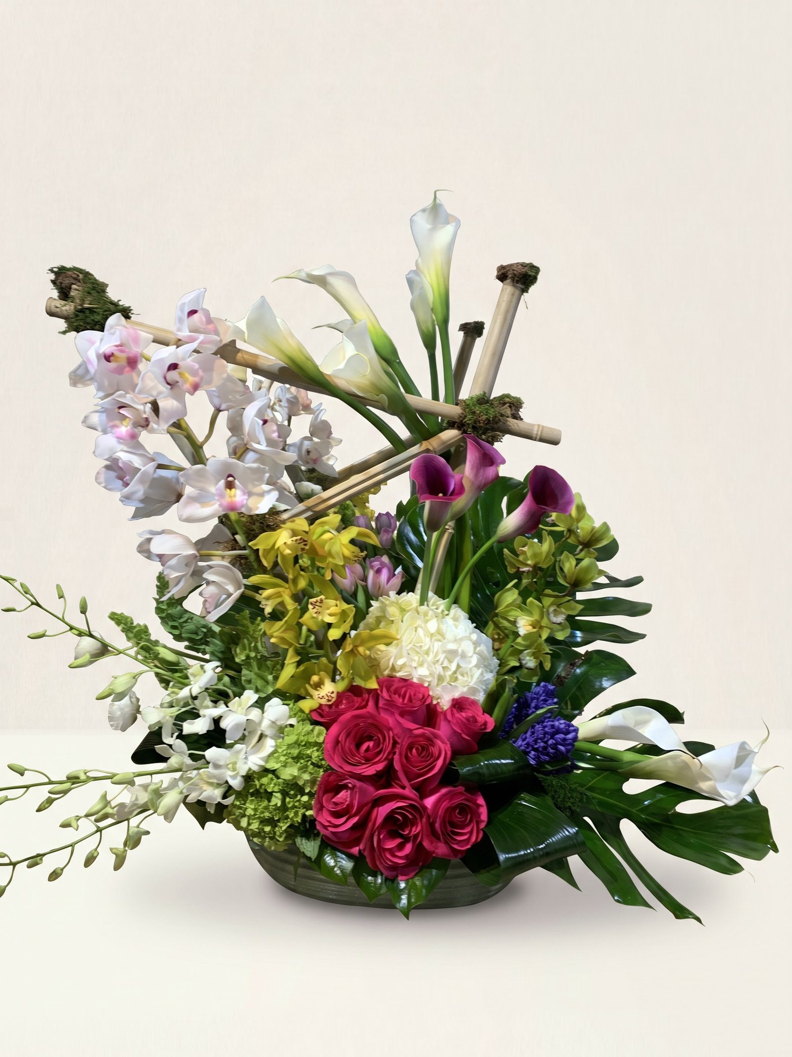 Arreglo escultural de calas blancas y moradas y orquídeas cymbidium blancas sobre bambú