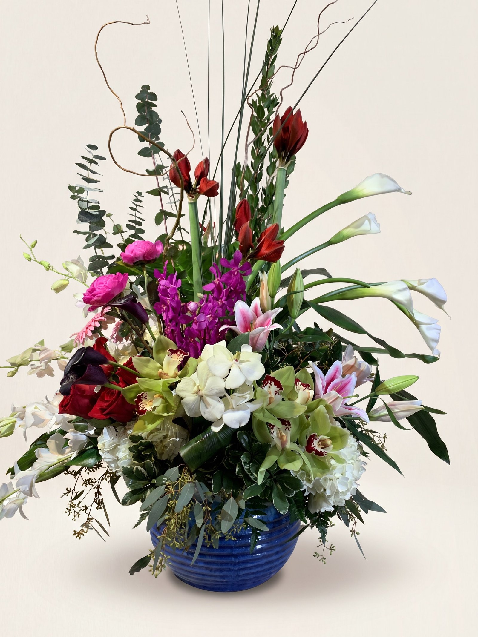 Red amaryllis, white calla lilies, and fuchsia roses in a cobalt-blue ceramic bowl