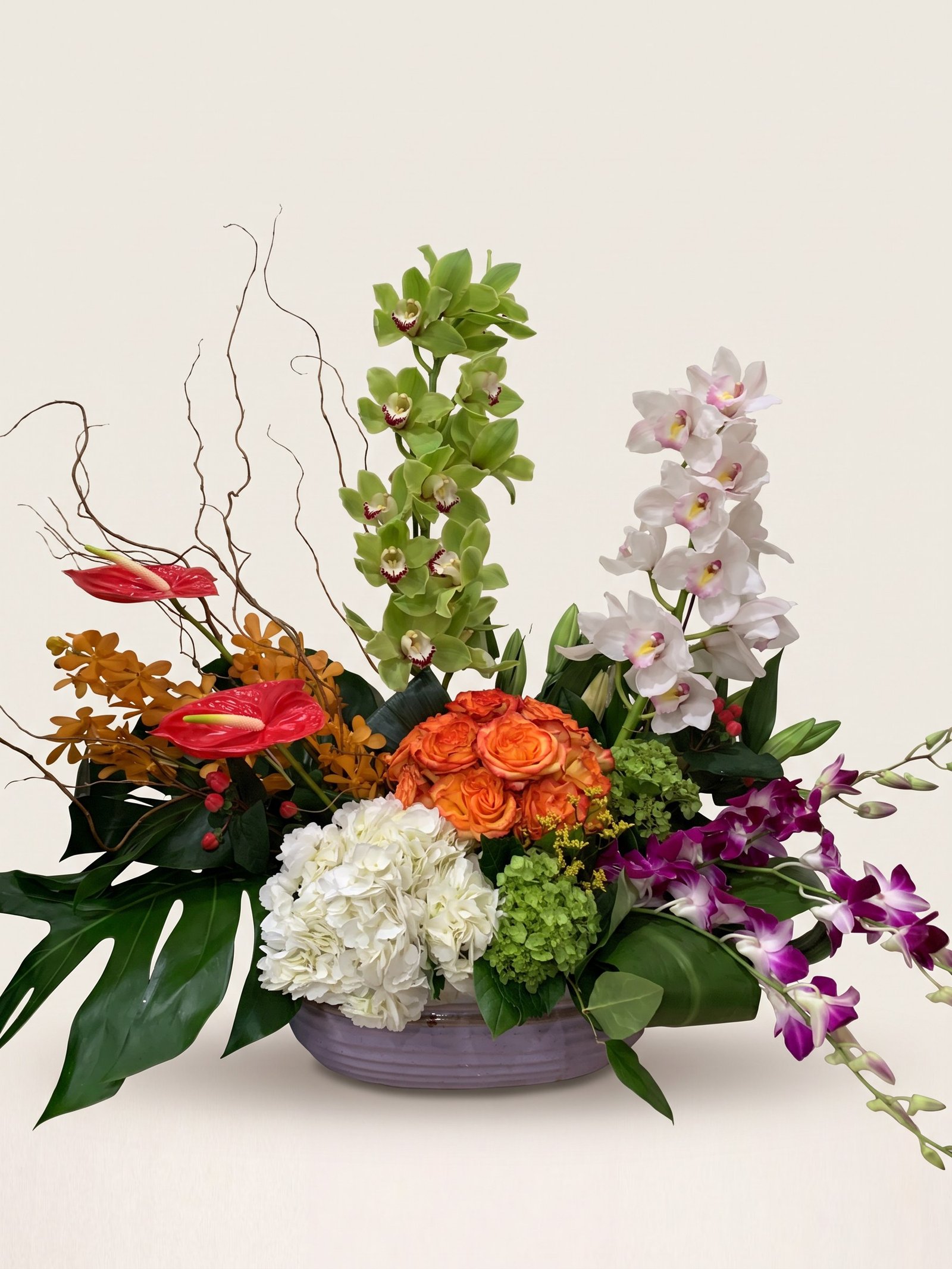 Centerpiece of green and white cymbidium orchids, a pink peony, and orange roses in a ceramic bowl