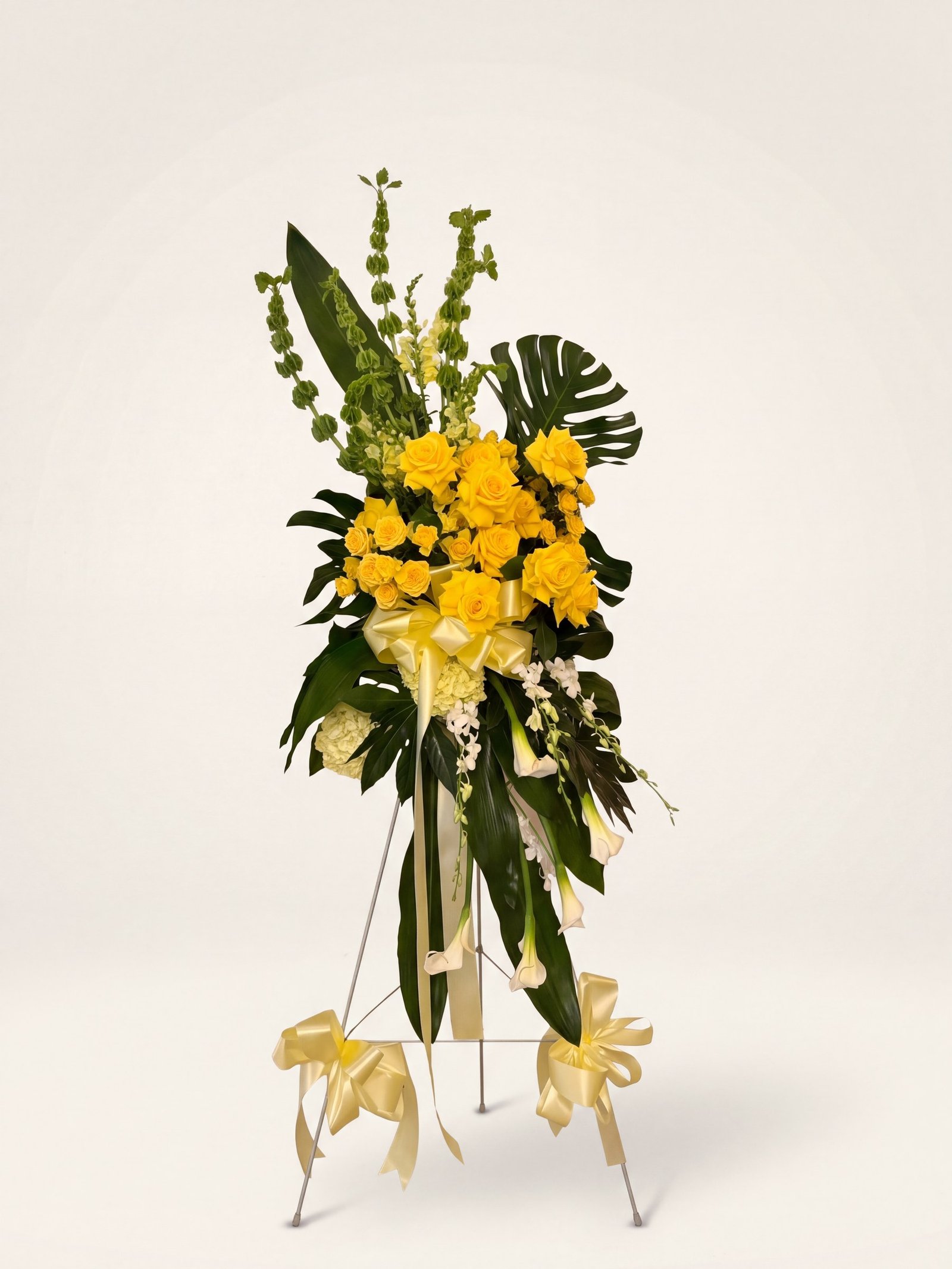 Standing funeral spray of yellow roses with bells of Ireland and monstera leaves on an easel