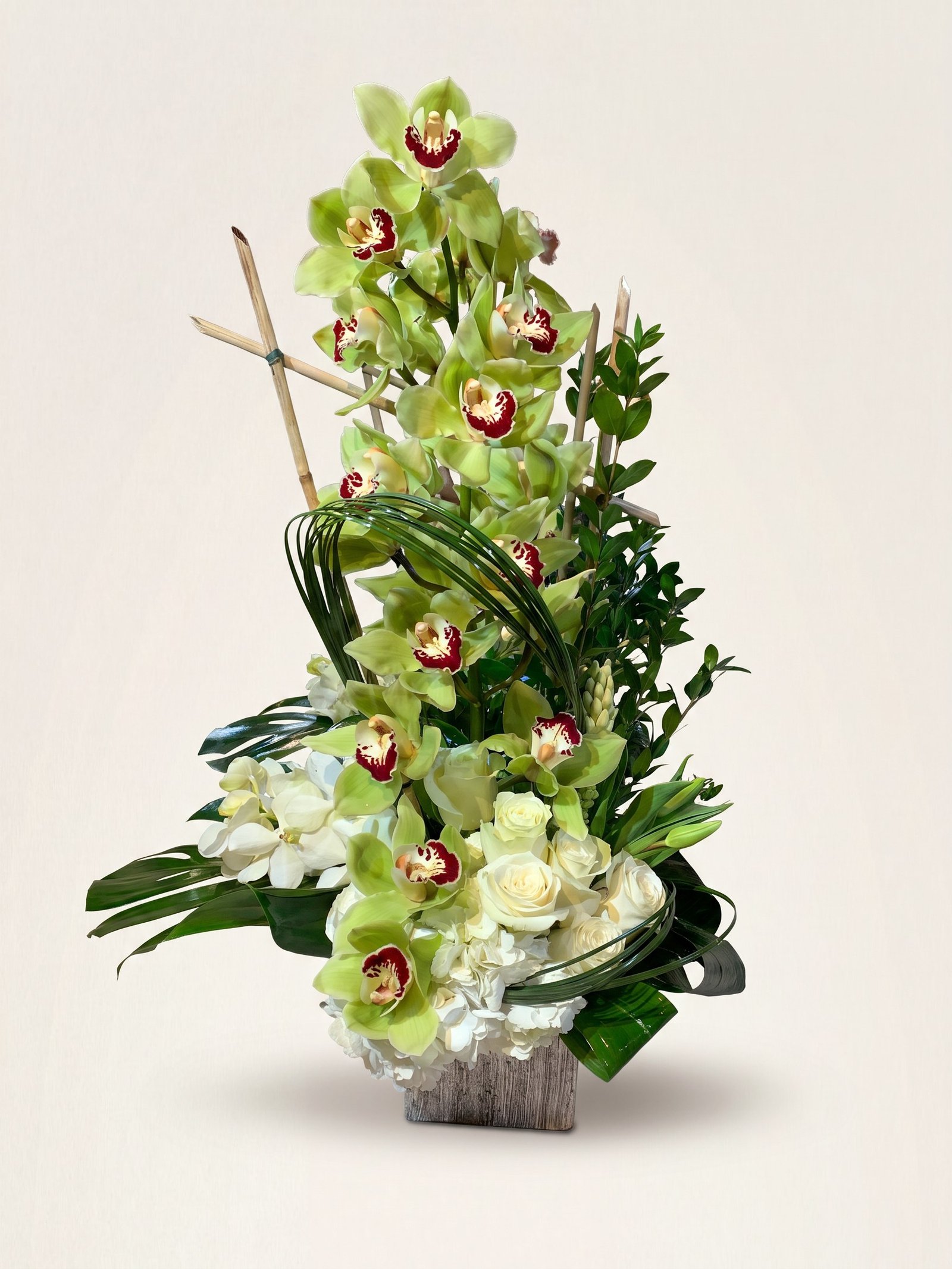 Tall sympathy arrangement of green cymbidium orchids and white roses on a silver base