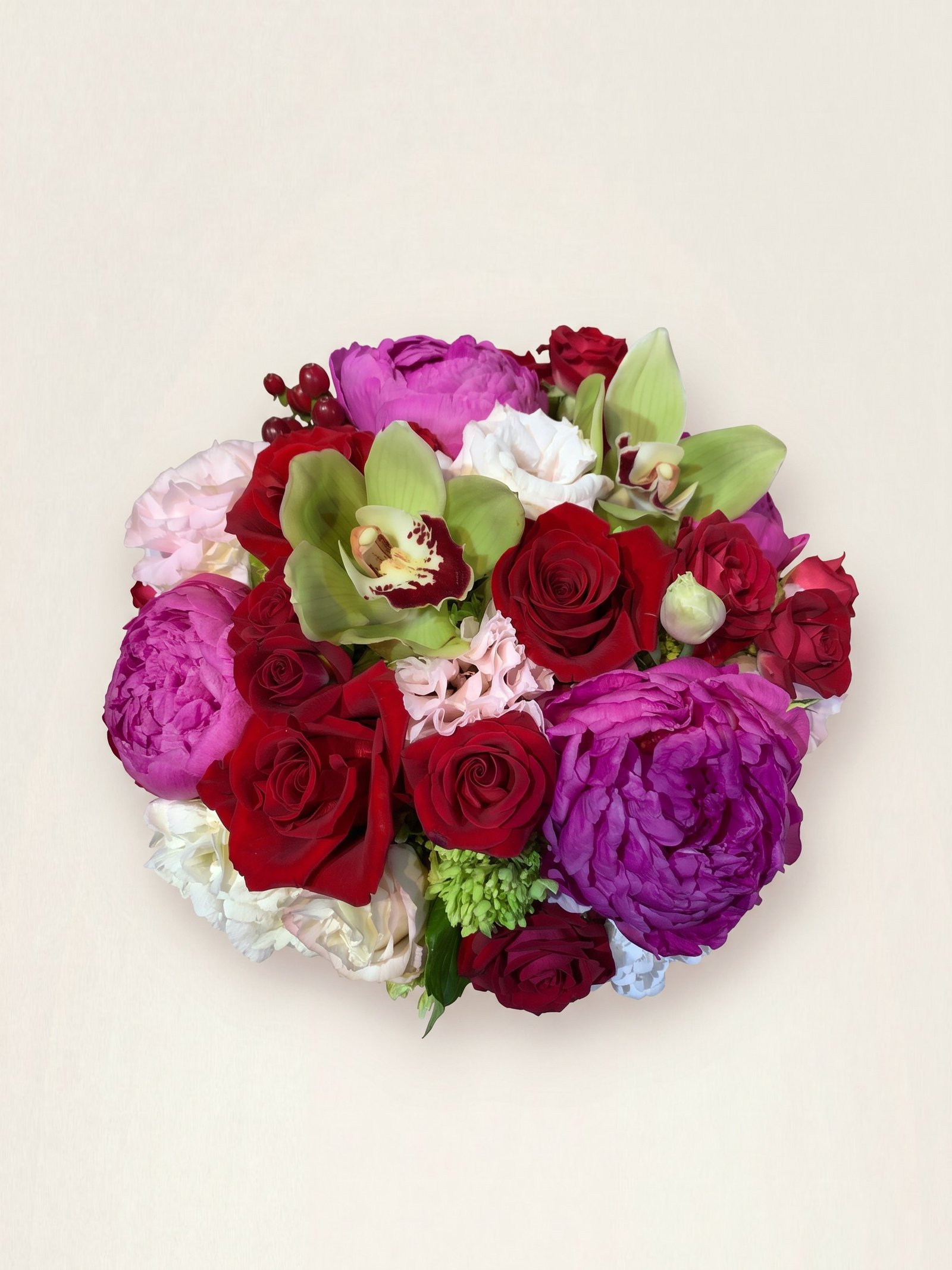 Compact arrangement of fuchsia peonies, red roses, and green cymbidium orchids seen from above