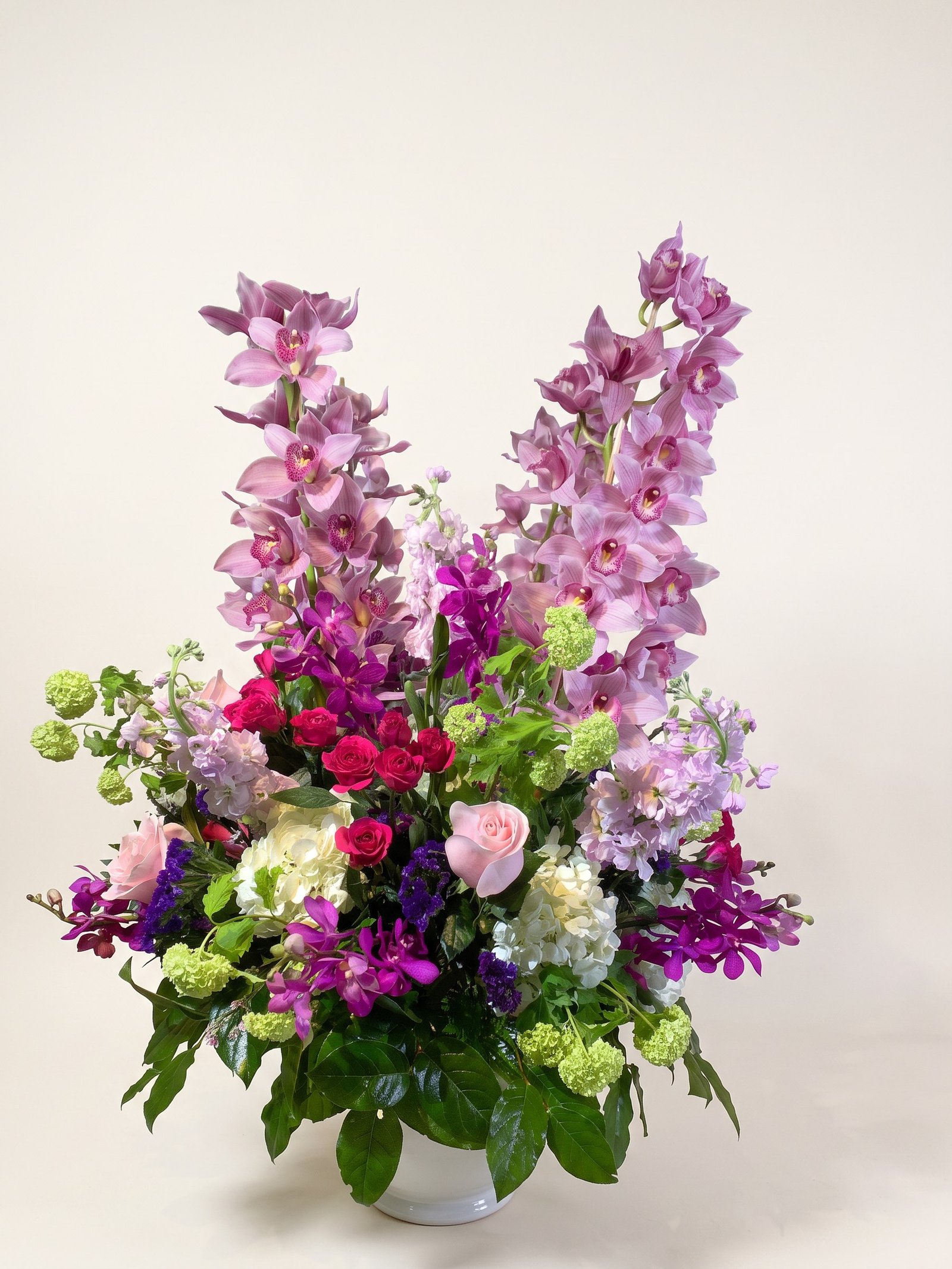 Orquídeas cymbidium altas lavanda con rosas rosadas y fucsia en jarrón blanco