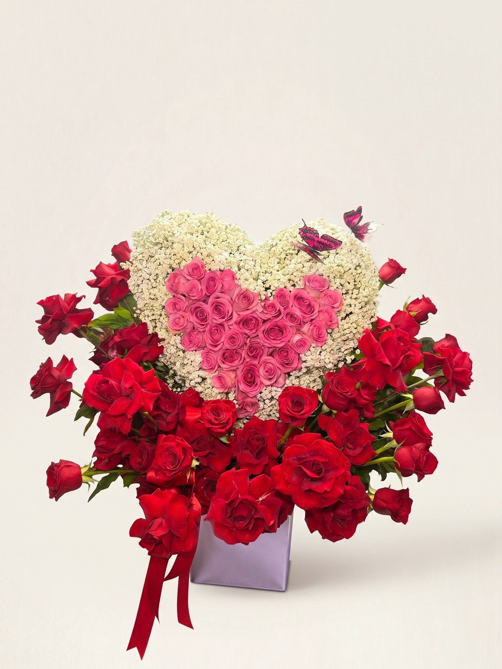Heart of pink roses with a white baby's breath border over a mass of red roses, with a red satin bow in a silver cube