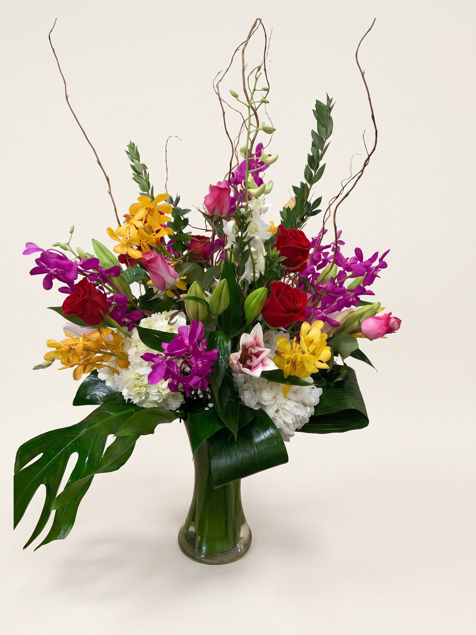 Orquídeas dendrobium moradas y mokara amarillas con rosas rojas en jarrón alto de vidrio