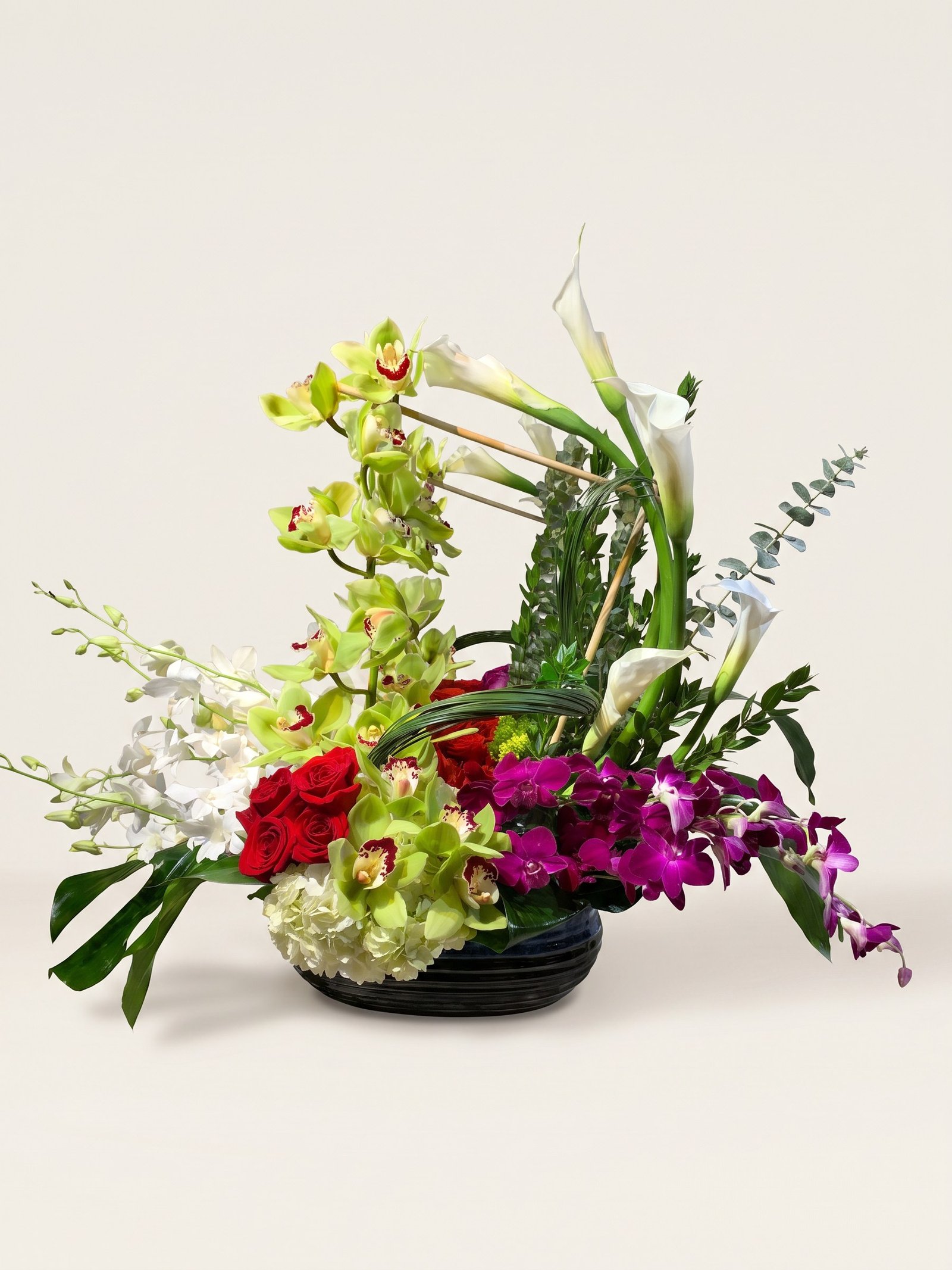Green cymbidium orchids, white calla lilies, and red roses with bamboo in a glossy black bowl
