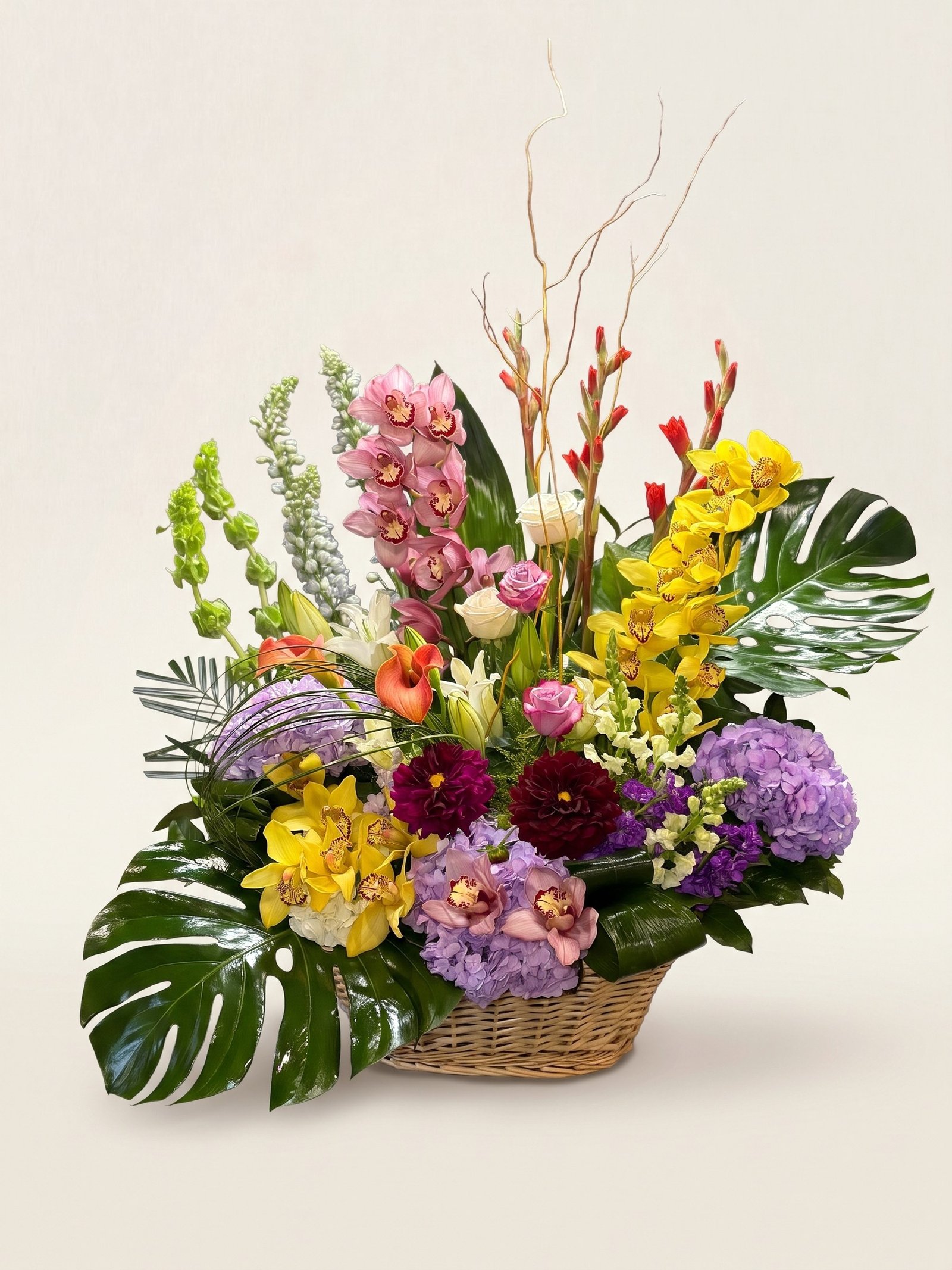 Large wicker basket of pink and yellow cymbidium orchids, gladiolus, dahlias, calla lilies, and bells of Ireland