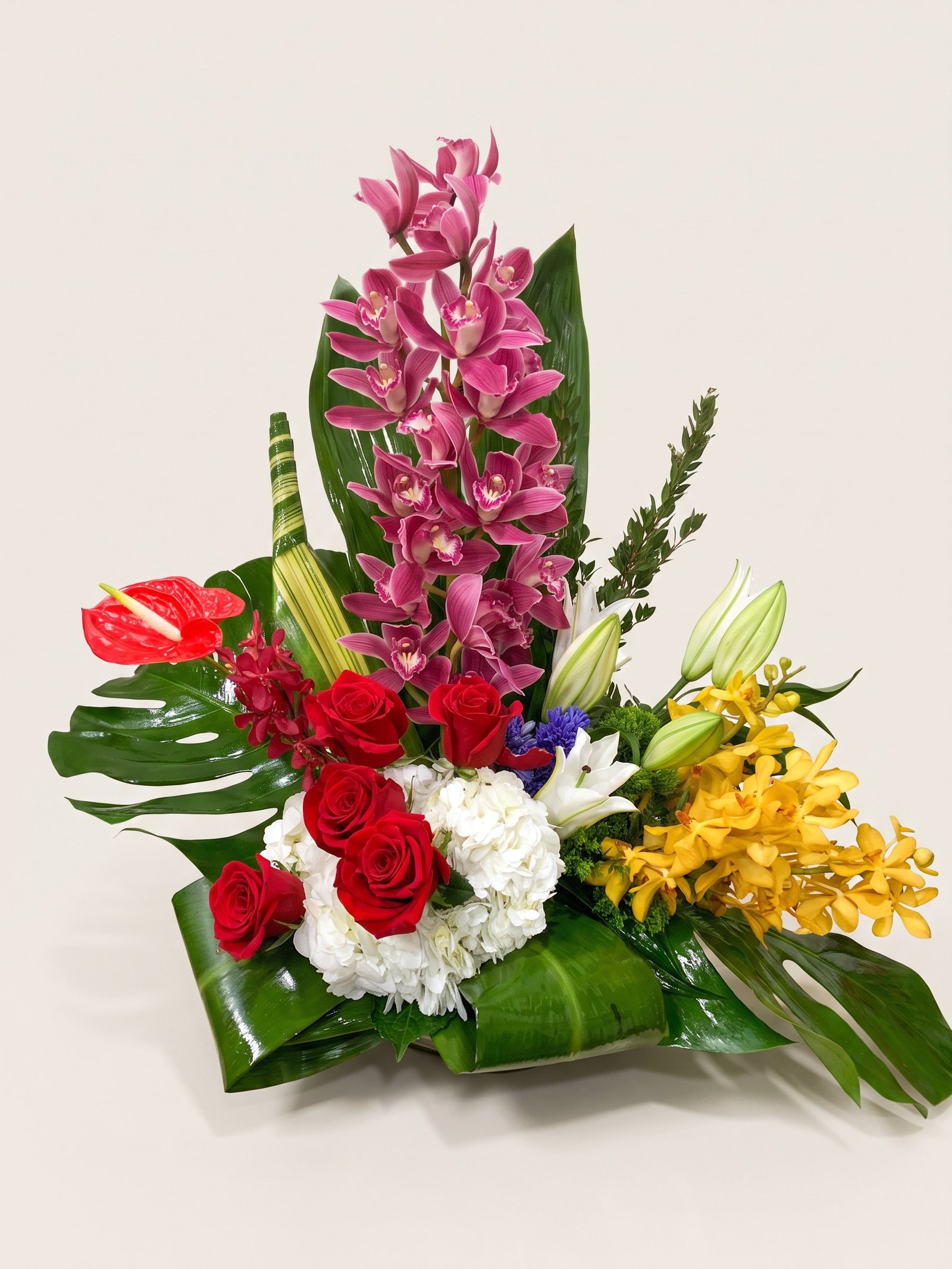 Tall magenta cymbidium orchid with red anthurium and red roses