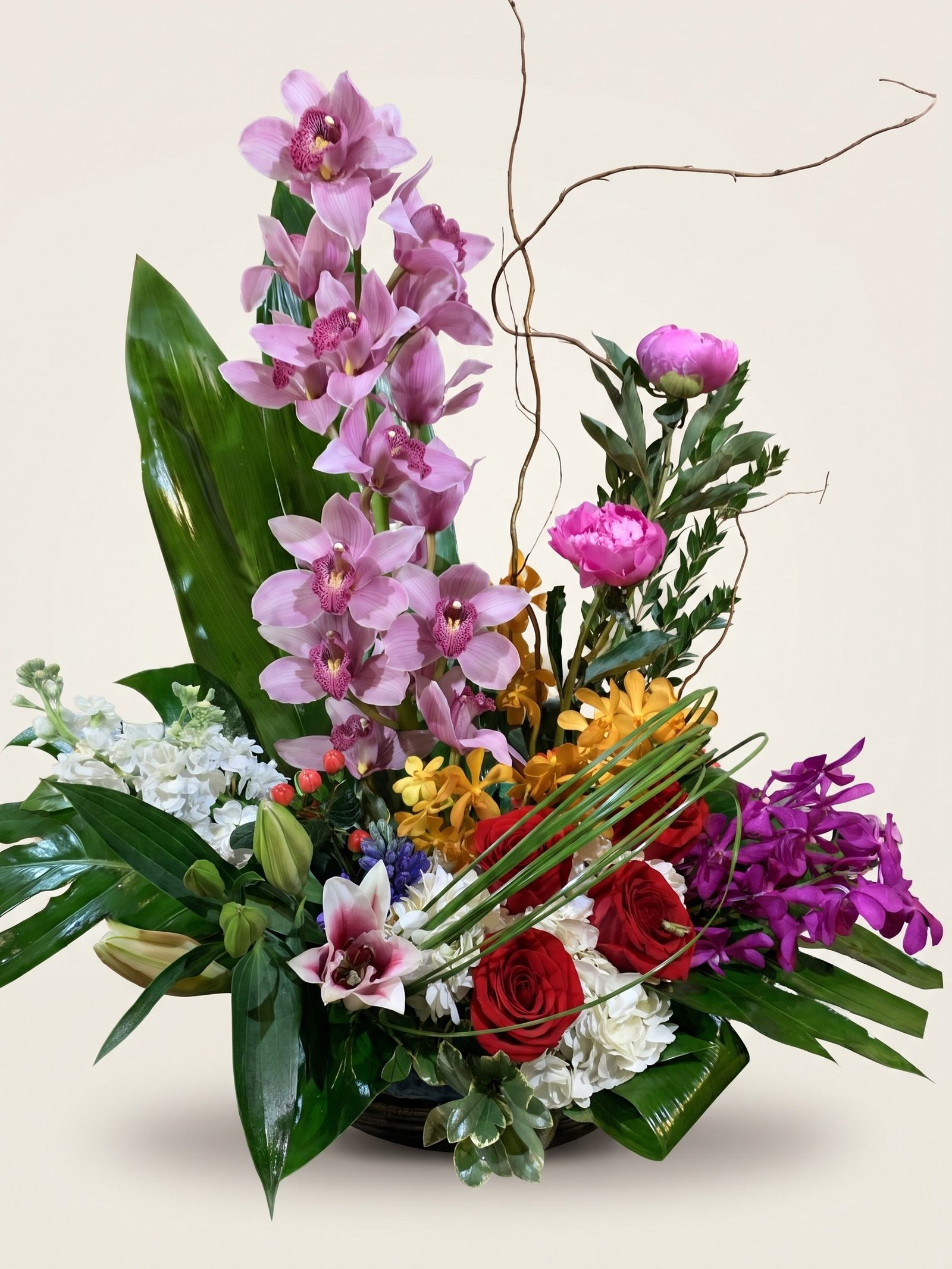 Arching pink cymbidium orchid with a pink lily, a peony, and red roses