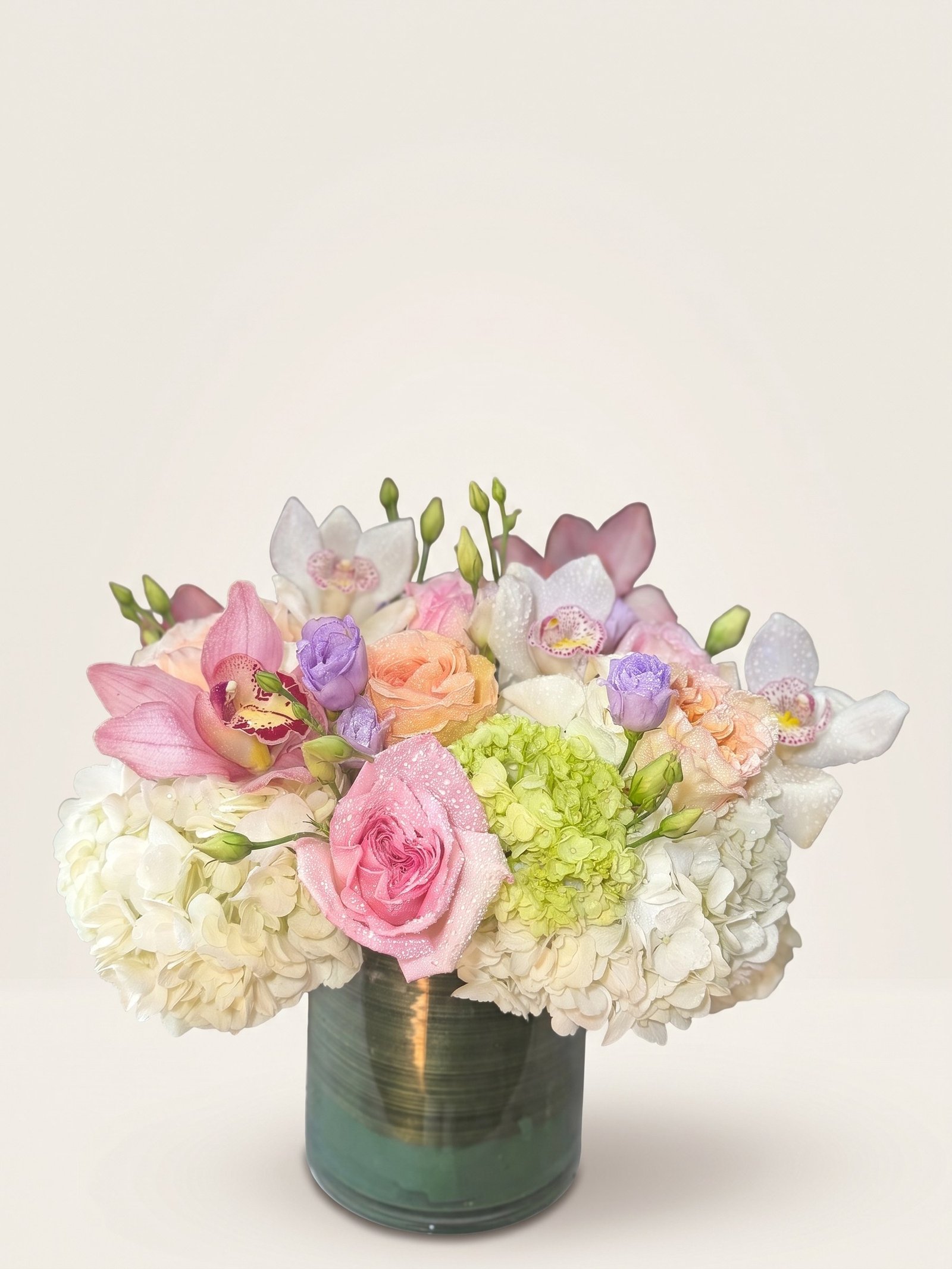 Pastel arrangement of white hydrangea, pink garden roses, and pink and white cymbidium orchids in a green cylinder, second view