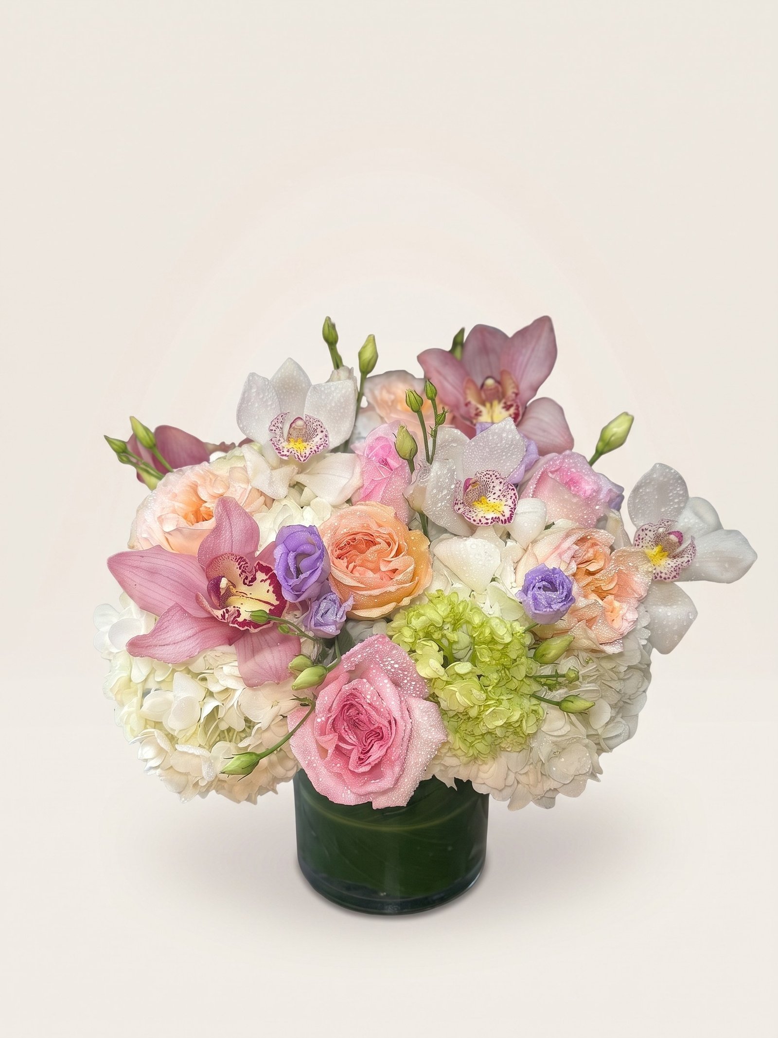 Pastel arrangement of white hydrangea, pink garden roses, and pink and white cymbidium orchids in a green cylinder