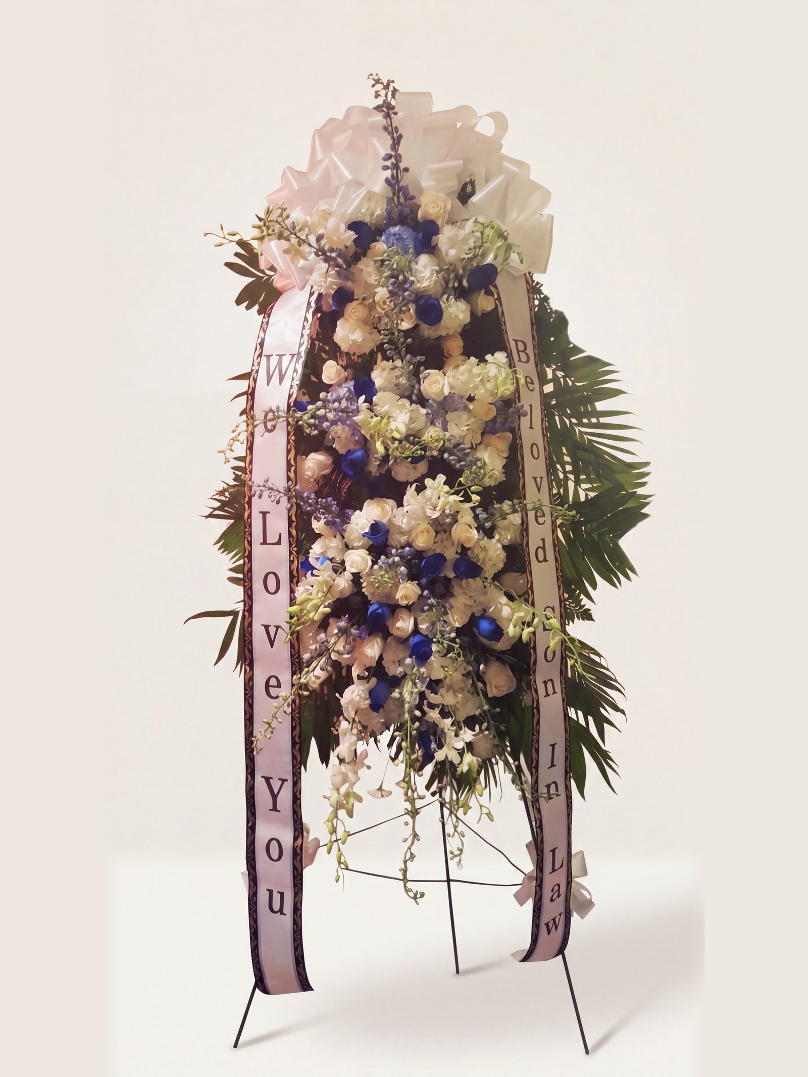 Tall blue-and-white funeral tribute of roses with hand-lettered sashes on an easel