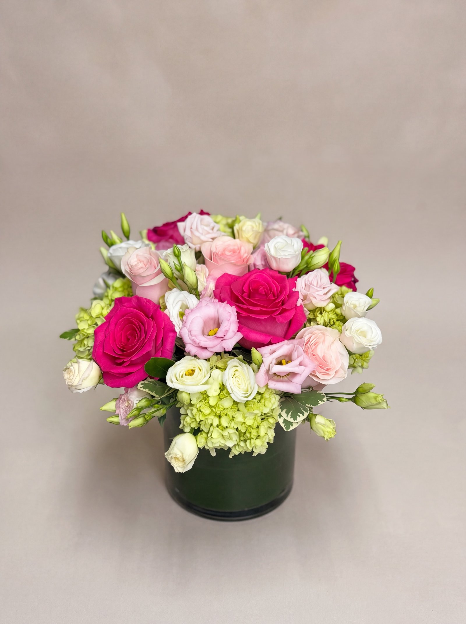 Hot pink roses and green hydrangea in a deep green ceramic cylinder