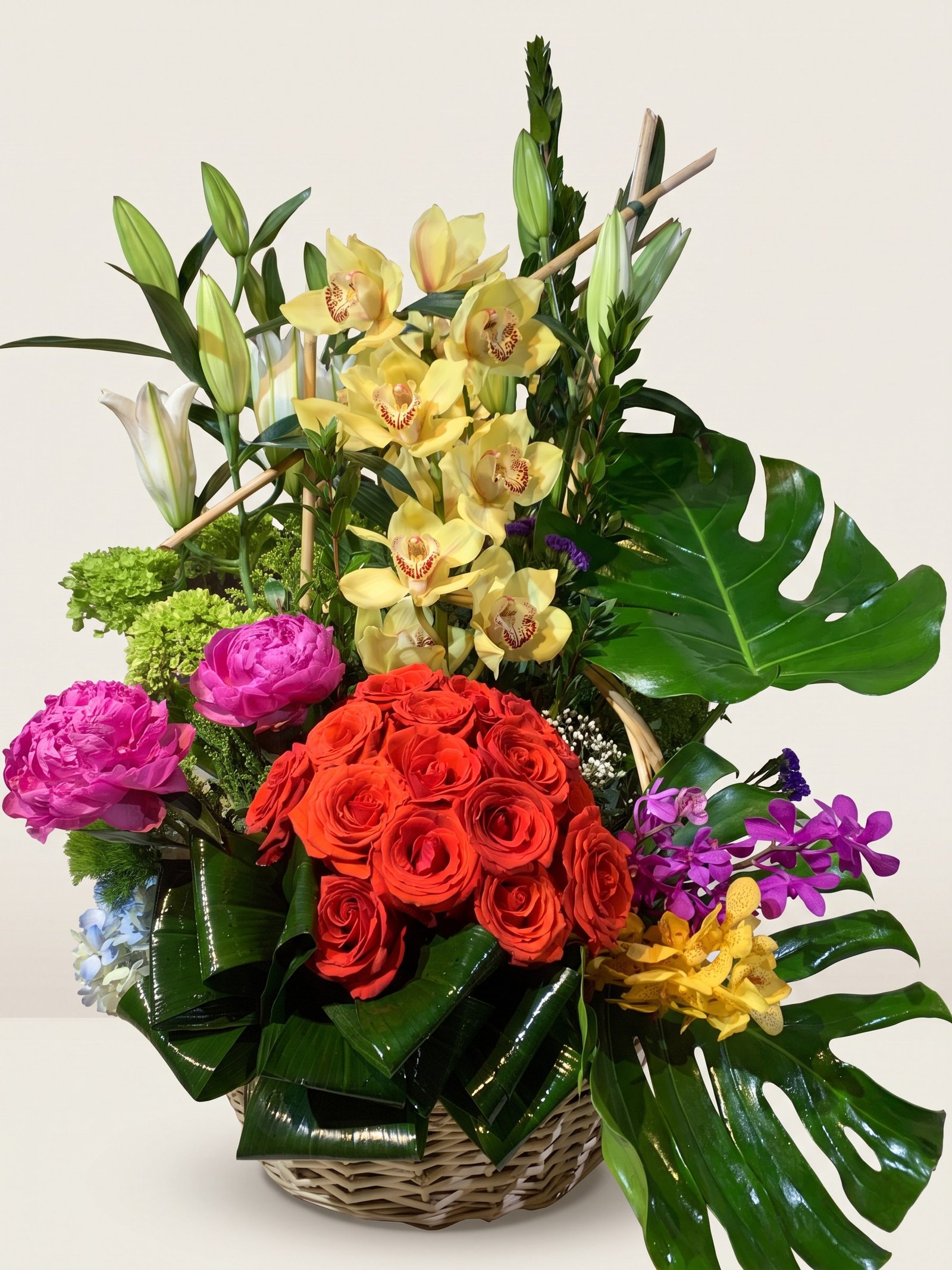 Cesta de mimbre con orquídeas cymbidium amarillas, rosas naranja, peonías fucsia y bambú