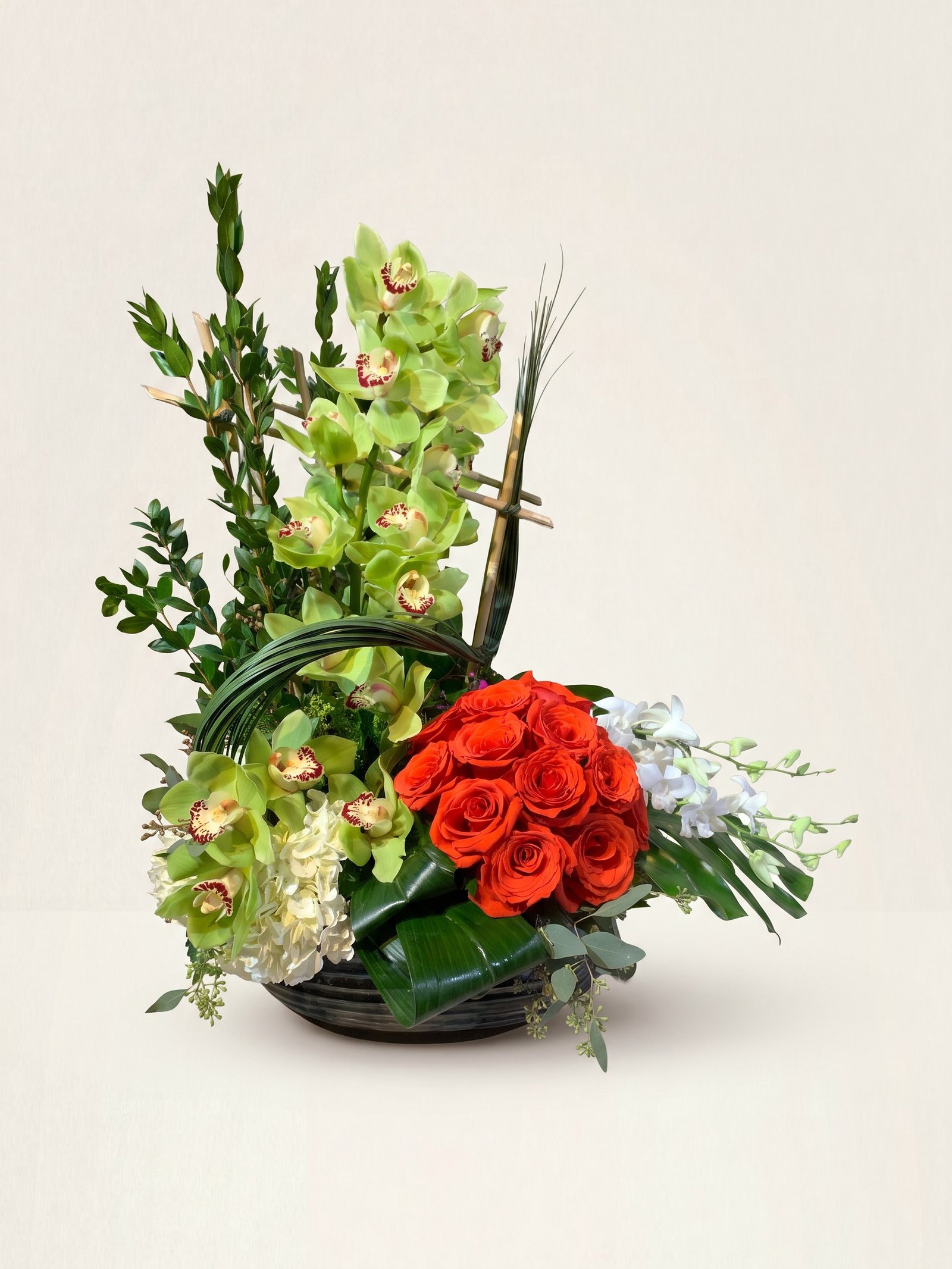 Orquídeas cymbidium verdes sobre rosas naranja rojizo y dendrobium blanco en cuenco bajo oscuro