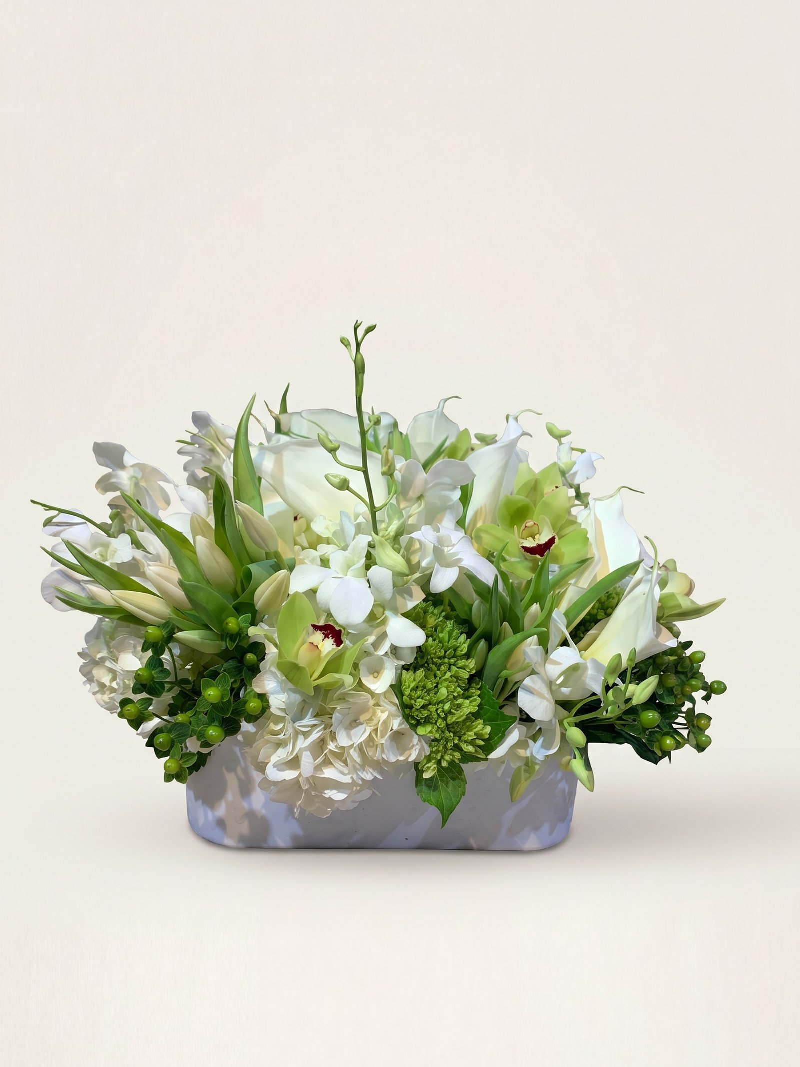Arreglo bajo blanco y verde de orquídeas cymbidium, calas y lirios en recipiente blanco